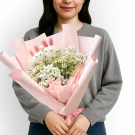 Woman holding a bouquet of white daisies, baby's breath, and two bunny-shaped ping pong mums wrapped in pink paper.