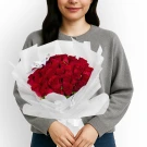 Woman in gray sweater holding a large bouquet of 30 red roses wrapped in white paper.