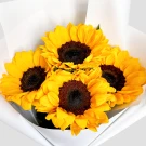 Four bright yellow sunflowers with dark centers, wrapped in white paper.
