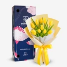 A bouquet of 10 bright yellow tulips with green leaves, wrapped in cream and yellow paper, tied with a yellow ribbon.