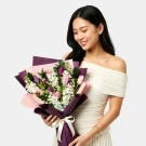 Woman holding a bouquet of purple and pink tulips with white flowers, wrapped in deep purple paper and tied with a white ribbon.