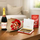 Champagne, strawberry bouquet, and chocolate boxes on a table.