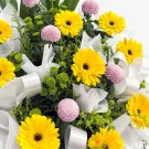 Yellow gerberas and pink mums in a white floral arrangement.