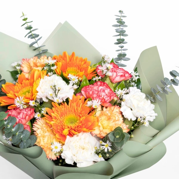 A vibrant bouquet of orange gerberas and carnations with white accents, wrapped in pale green paper.