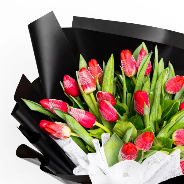 Bouquet of red tulips with green leaves, wrapped in black and white paper.