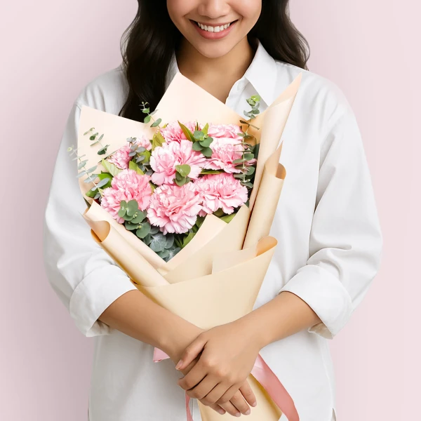 Woman in white shirt holding a bouquet of pink carnations and eucalyptus leaves.