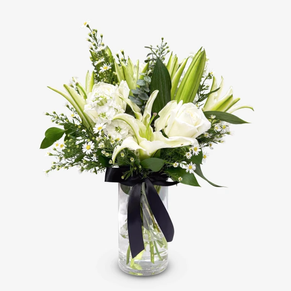 White lilies, roses, and matthiola in a glass vase with a black ribbon.