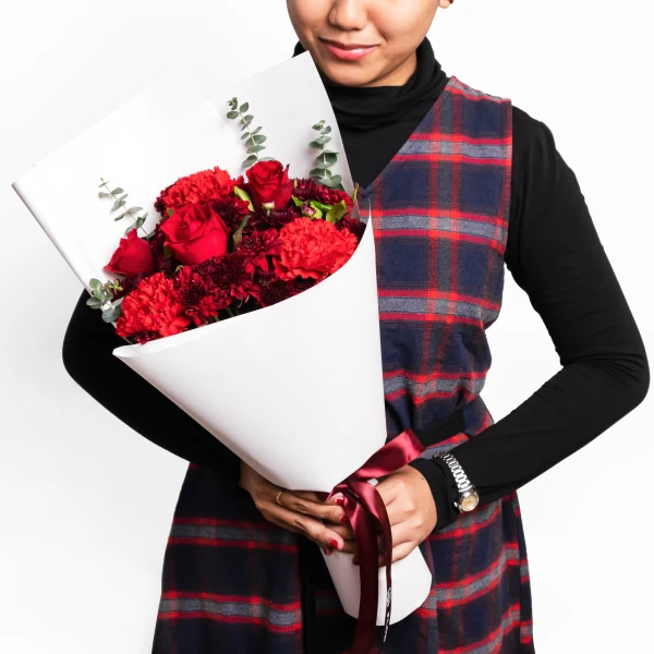 Woman holding a bouquet of red roses and carnations wrapped in white paper, wearing a plaid dress.