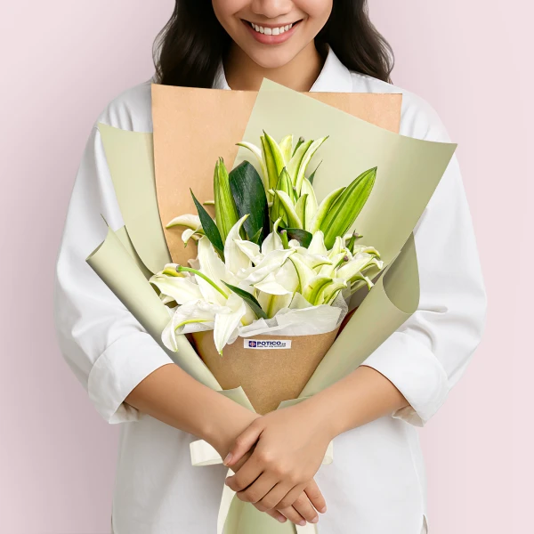 Woman in white holding a bouquet of white lilies wrapped in kraft paper and green paper.