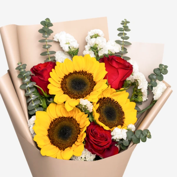 Red roses and sunflowers arranged in a neutral paper wrap, with eucalyptus and white filler flowers.