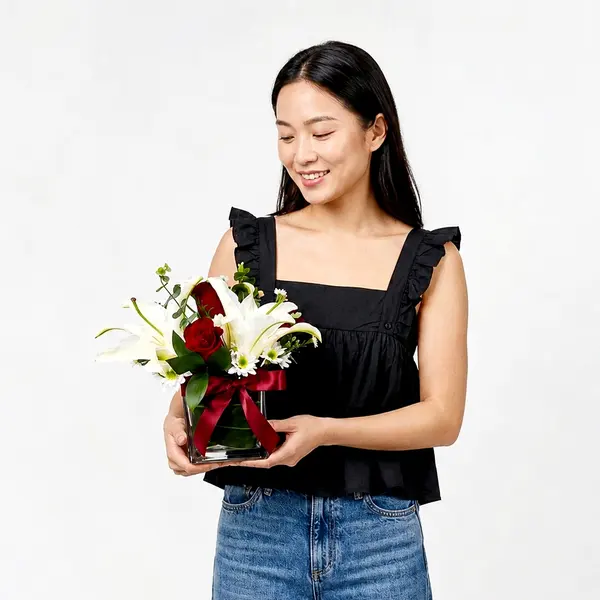 A lush arrangement of white lilies, red roses, and white chrysanthemums in a glass vase with a red ribbon.