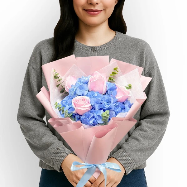 Pink roses and blue hydrangeas with eucalyptus in pink and white paper, tied with a blue ribbon.