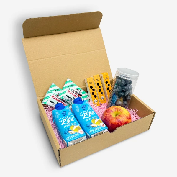 Cardboard box with coconut water, Fisherman's Friend, blueberries, apple, and candy.