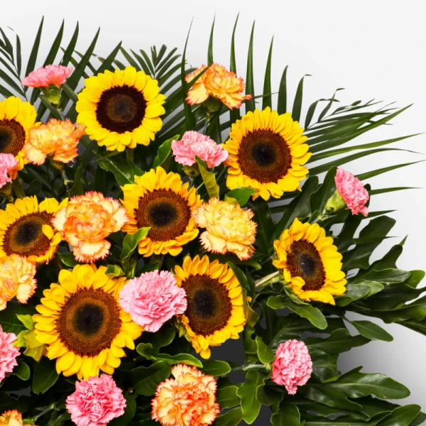 A vibrant floral arrangement featuring sunflowers, pink and orange carnations, and lush green foliage.