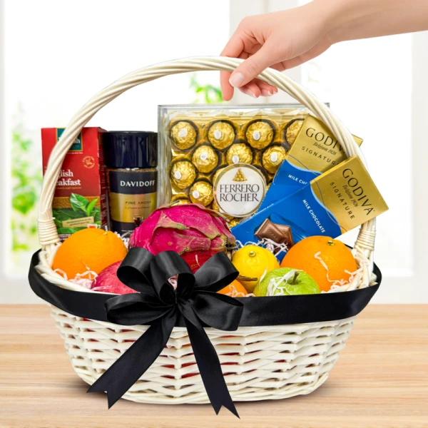 White wicker basket overflowing with fruits, Ferrero Rocher, Godiva chocolates, and Davidoff coffee.