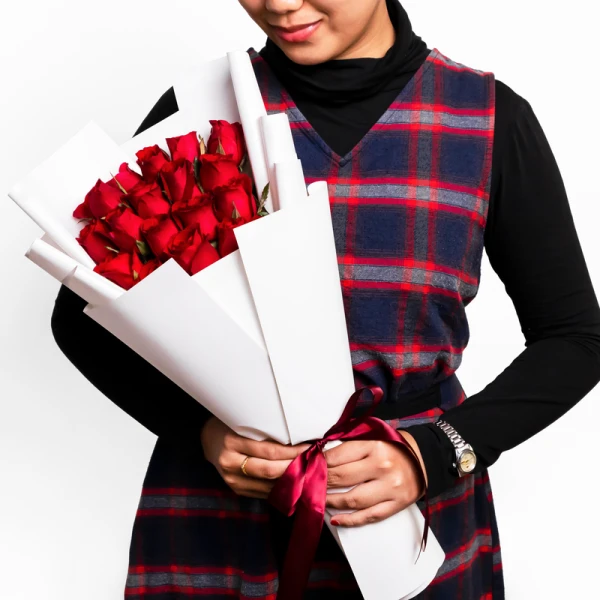 Woman in plaid dress holding a bouquet of 18 red roses wrapped in white paper with a burgundy ribbon.