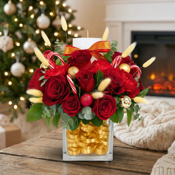Red roses, carnations, candy canes, gold ornaments, and a candle in a square vase with gold ribbon.