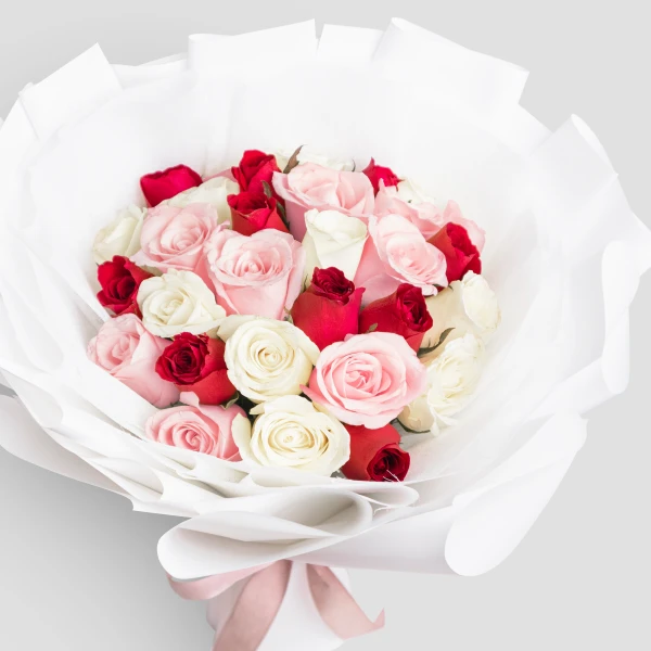 A bouquet of red, pink, and white roses wrapped in white paper with a pink ribbon.