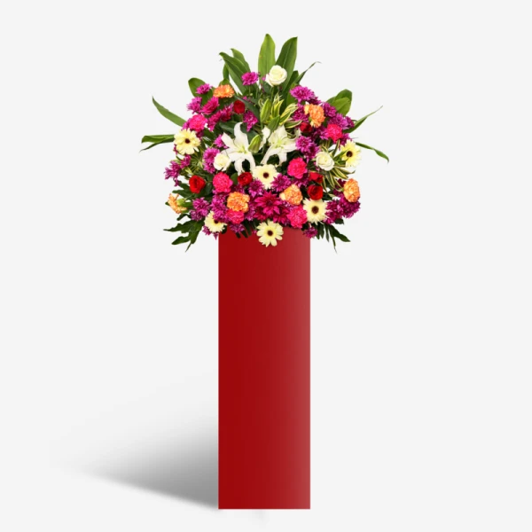 Grand floral arrangement with white lilies, red and white roses, and carnations on a red stand.