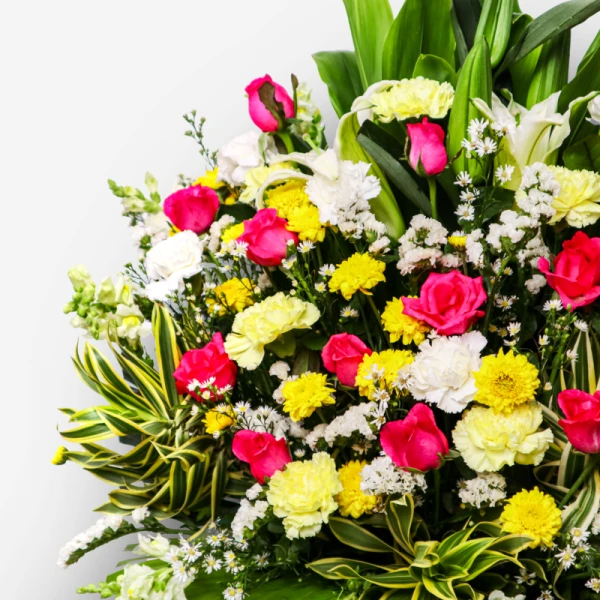 Floral sympathy stand with pink roses, yellow and white carnations, white lilies, and mums.