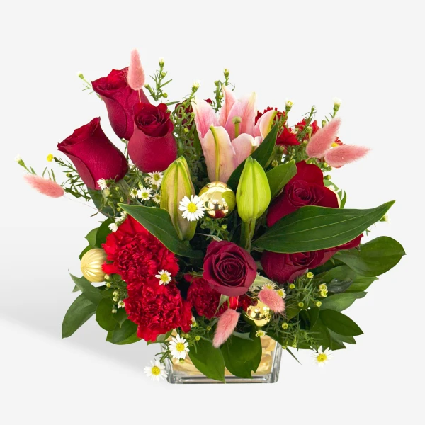 Red roses, lilies, and carnations with gold ornaments in a clear vase.