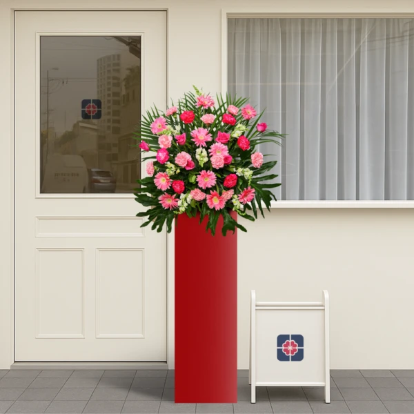 Pink Jubilee flower arrangement on a red stand, in front of a door and window.