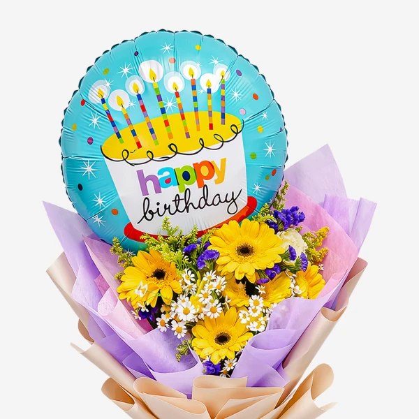 A birthday balloon with a cake design sits atop a bouquet of yellow gerbera daisies and small white flowers.