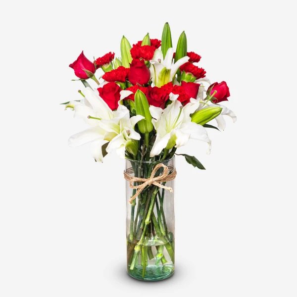 Red roses, white lilies, and red carnations in a clear vase tied with twine.