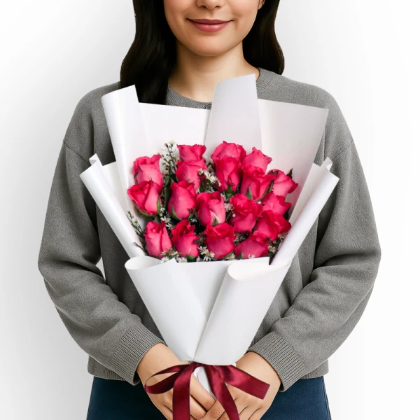 Bouquet of 18 pink roses with white accents, held by a person wearing a grey sweater and a maroon ribbon at the base.