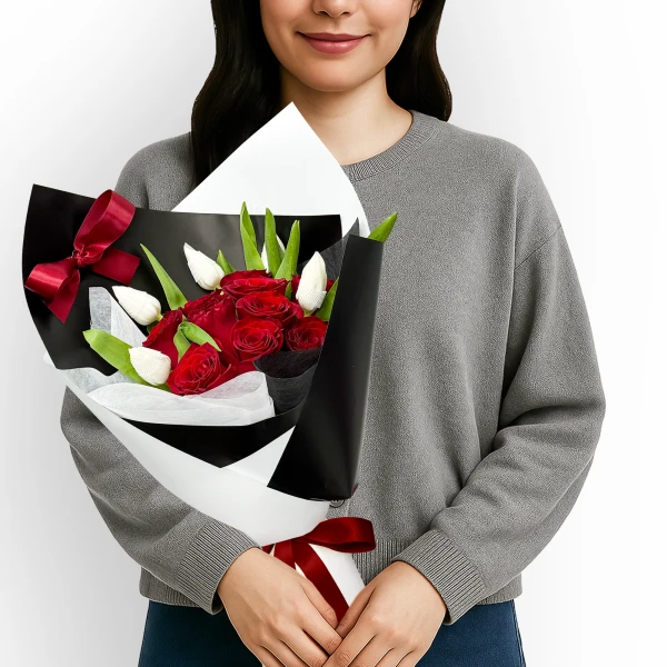 Woman in grey sweater holding a bouquet of red roses and white tulips, tied with red ribbon.
