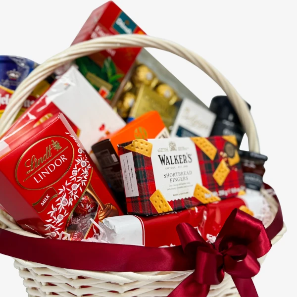 Gourmet gift basket overflowing with chocolates, cookies, and candies, tied with a red ribbon.