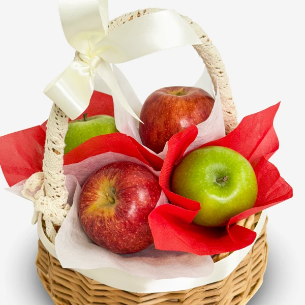 A woven basket filled with red and green apples, decorated with a cream ribbon and red and white tissue paper.