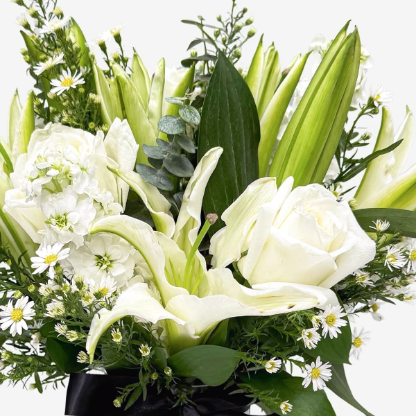 White lilies, roses, and matthiola with greenery in a black-ribboned arrangement.