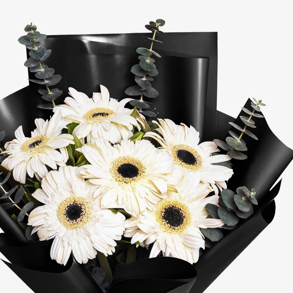 White gerbera daisies and eucalyptus stems in a black paper wrap.