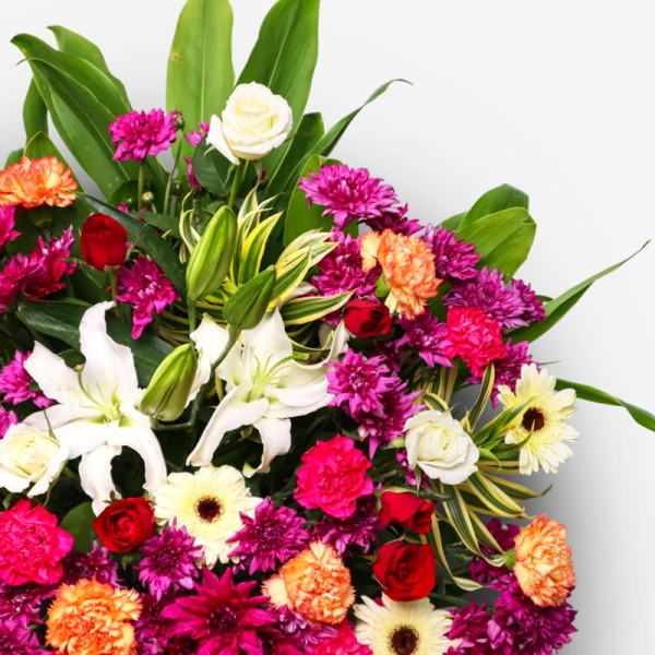 Close-up of a vibrant floral arrangement with white lilies, roses, gerberas, carnations, and mums.
