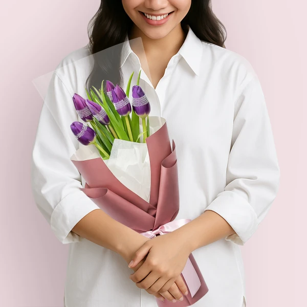 Woman in white shirt holding purple tulips decorated with rhinestones, wrapped in pink paper.