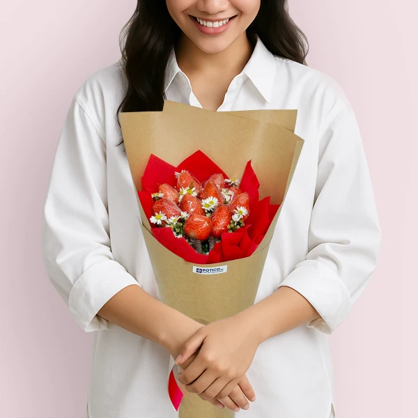 Woman in white shirt holding a strawberry bouquet with red paper and daisies.