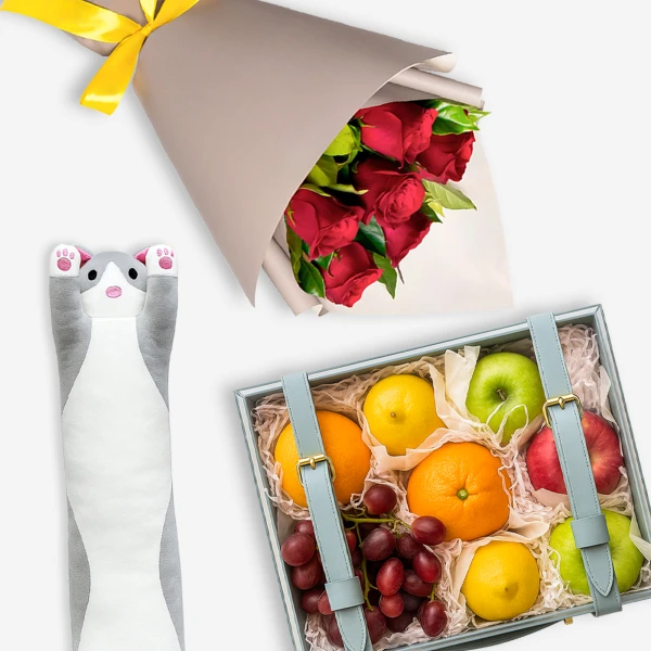 A gift box of fruits, red roses, and a plush cat toy, tied with a yellow ribbon.
