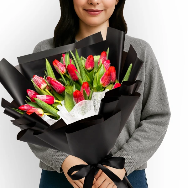 Woman holding a bouquet of 20 red tulips wrapped in black paper, tied with a black ribbon.
