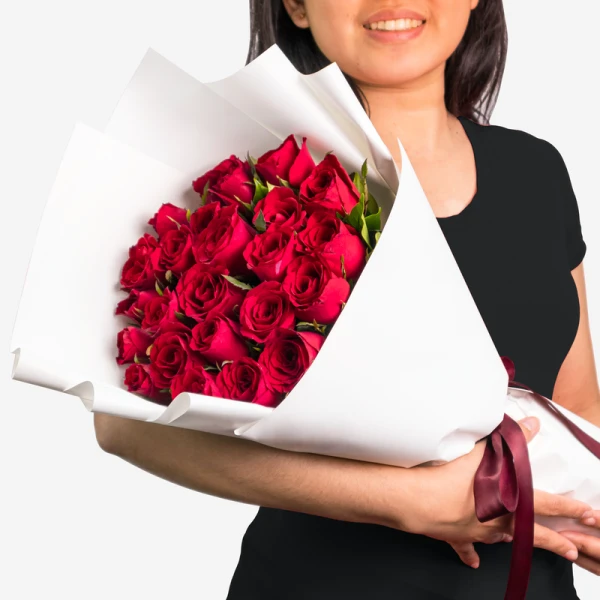 Woman holding a large bouquet of 24 vibrant red roses wrapped in white paper.