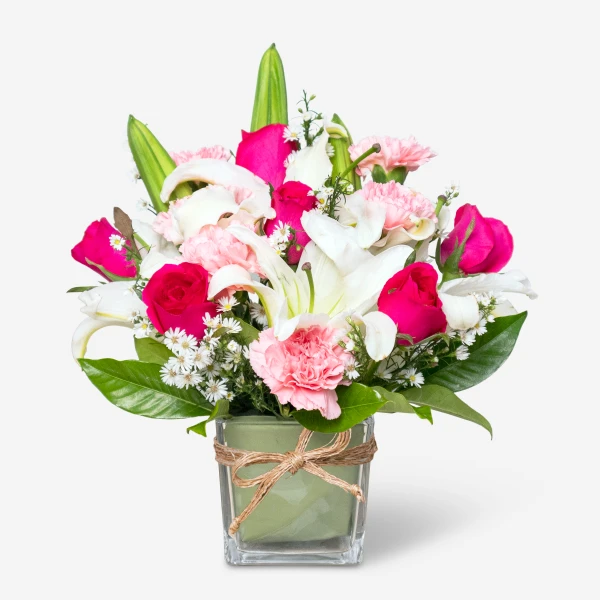Pink and white flowers including lilies and roses in a green glass vase tied with twine.