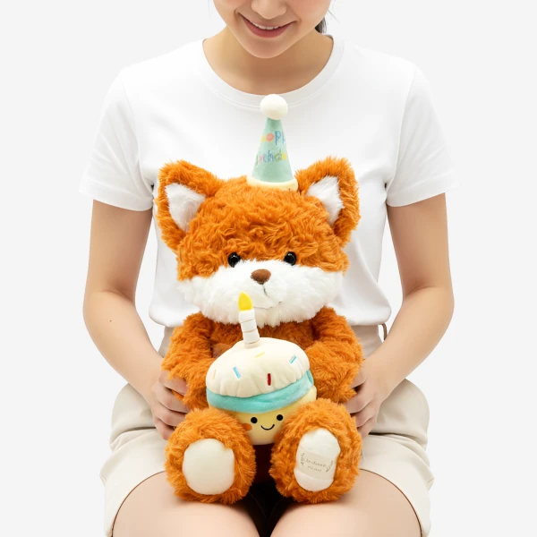 A plush fox wearing a party hat holds a cupcake with a candle.