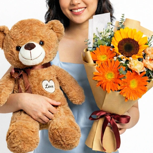 A person holds a teddy bear and an 'Oh, Honey' bouquet with sunflowers, gerberas, and carnations.