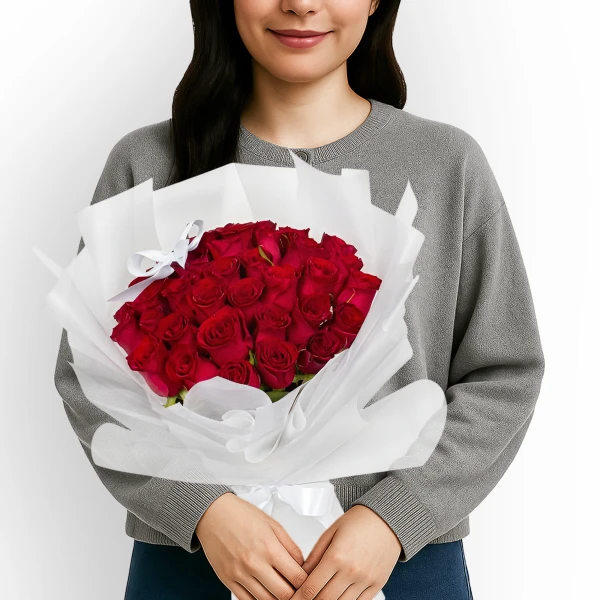 Woman in gray sweater holding a large bouquet of 30 red roses wrapped in white paper.