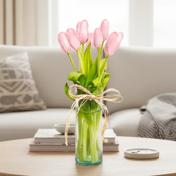 Pink tulips in a clear glass vase tied with a twine bow, sitting on a wooden table.