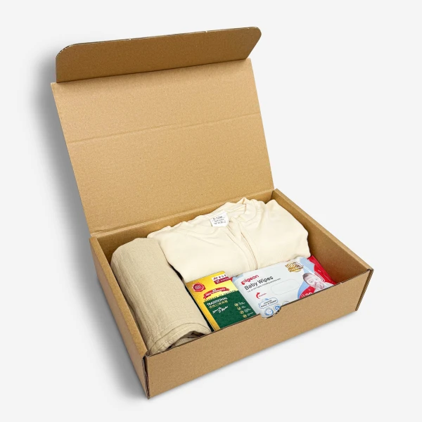 Open cardboard box with baby clothes, swaddle, chicken essence, and wet wipes.
