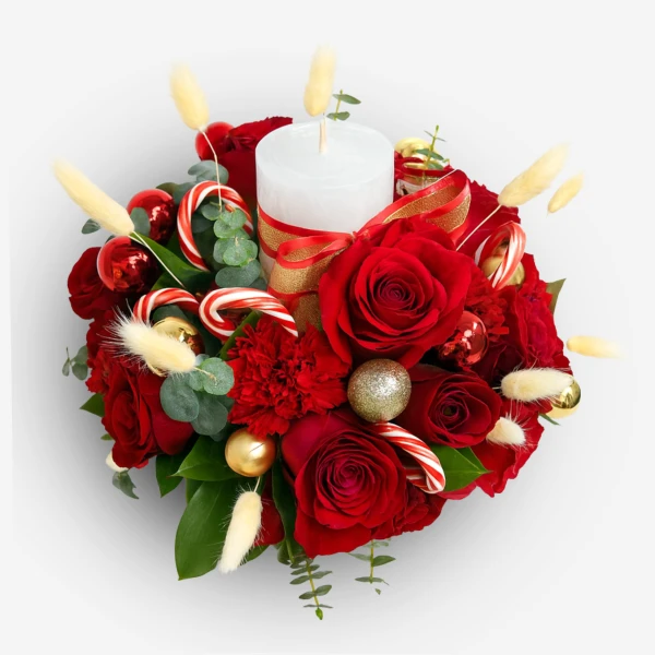 Christmas floral arrangement with red roses, carnations, candy canes, ornaments, and a white candle.