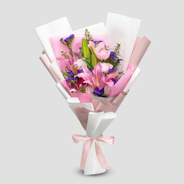 Pink stargazer lilies, roses, and purple statice in a bouquet wrapped in pink and white paper with a pink ribbon.