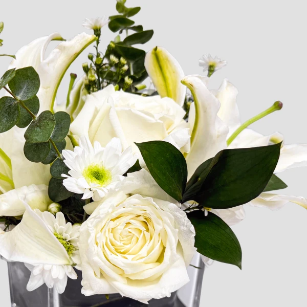 White roses, lilies, and daisies with greenery in a vase.