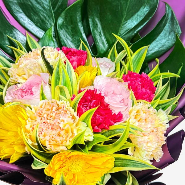 A bright floral bouquet with yellow, pink, and fuchsia flowers and green leaves.